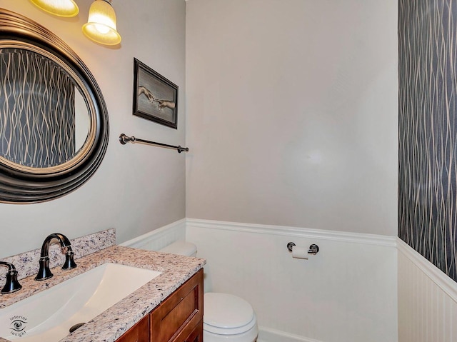 bathroom featuring vanity, a wainscoted wall, and toilet