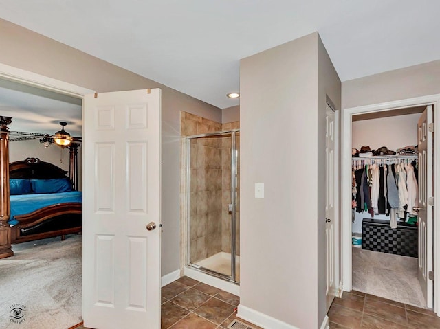 ensuite bathroom featuring a walk in closet, a shower stall, baseboards, tile patterned floors, and ensuite bathroom