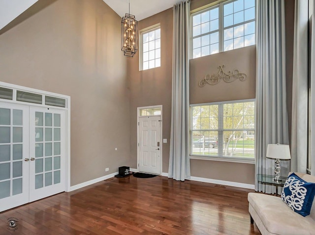 foyer entrance with wood-type flooring, a chandelier, a wealth of natural light, and a towering ceiling
