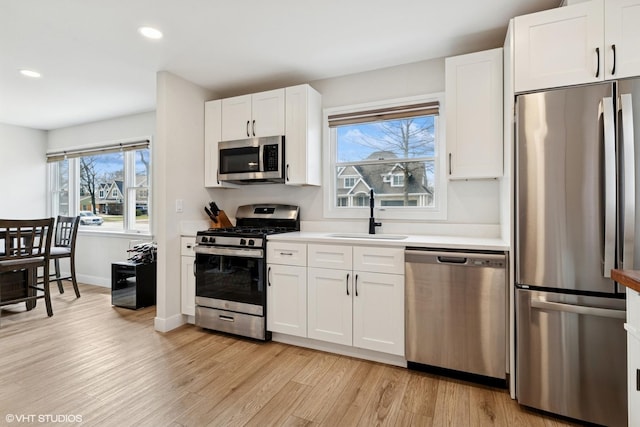 kitchen with a sink, stainless steel appliances, recessed lighting, white cabinetry, and light wood-type flooring