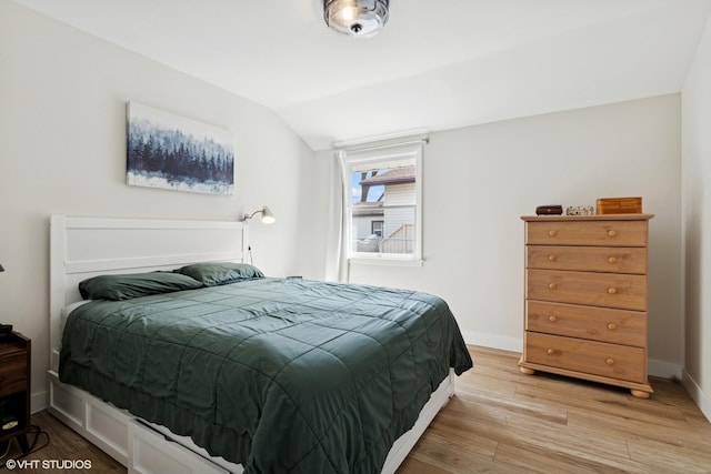 bedroom featuring baseboards, vaulted ceiling, and light wood-style floors