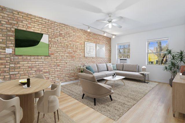 living area with a ceiling fan, brick wall, wood finished floors, track lighting, and baseboards