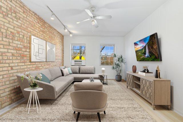 living area featuring ceiling fan, brick wall, rail lighting, baseboards, and light wood-style floors