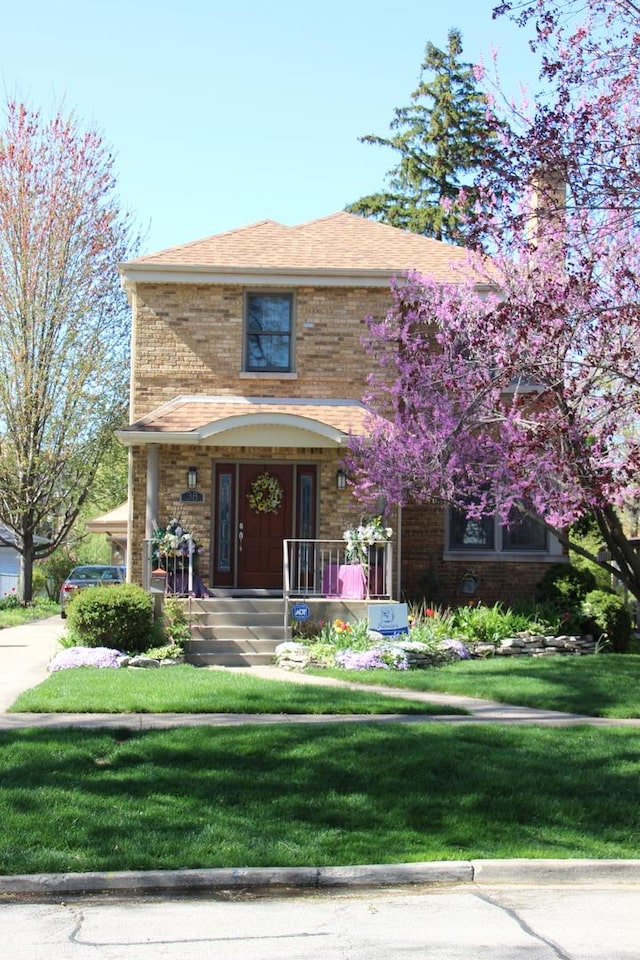view of front of property featuring brick siding, covered porch, and a front yard