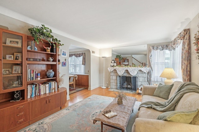 living room with baseboards, a stone fireplace, and light wood finished floors