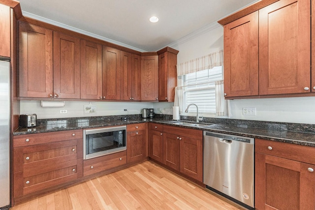 kitchen featuring appliances with stainless steel finishes, a sink, dark stone countertops, light wood-type flooring, and ornamental molding