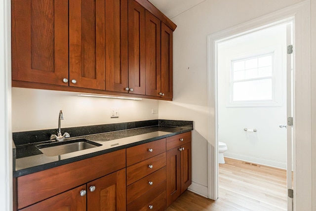 kitchen featuring visible vents, baseboards, light wood-type flooring, brown cabinets, and a sink