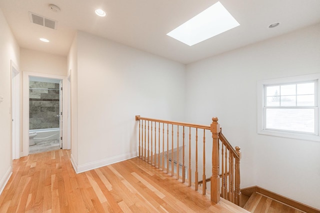 hall featuring a skylight, baseboards, light wood-style floors, and an upstairs landing