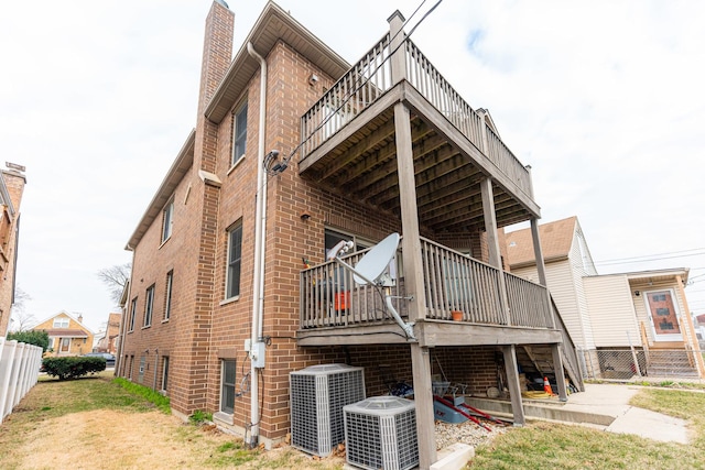 back of property featuring brick siding, central air condition unit, a chimney, and a deck