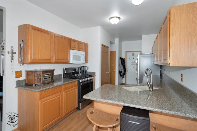 kitchen with appliances with stainless steel finishes, light stone counters, a sink, a peninsula, and light wood-type flooring