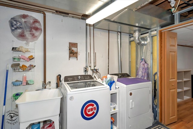 washroom featuring laundry area, washer and clothes dryer, a sink, and wood finished floors