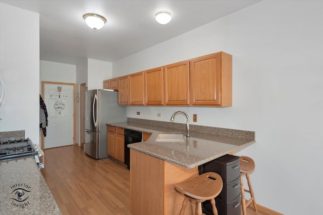kitchen featuring appliances with stainless steel finishes, a sink, light wood finished floors, a breakfast bar area, and a peninsula