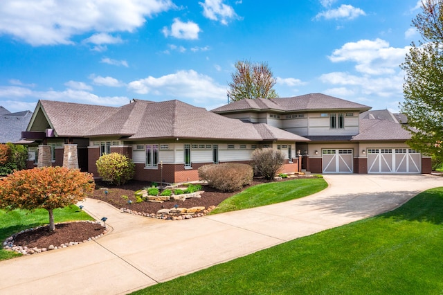prairie-style home with a shingled roof, a front yard, driveway, and brick siding