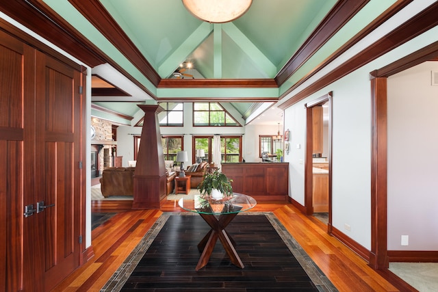 interior space featuring light wood finished floors, a fireplace, lofted ceiling, ornate columns, and ornamental molding