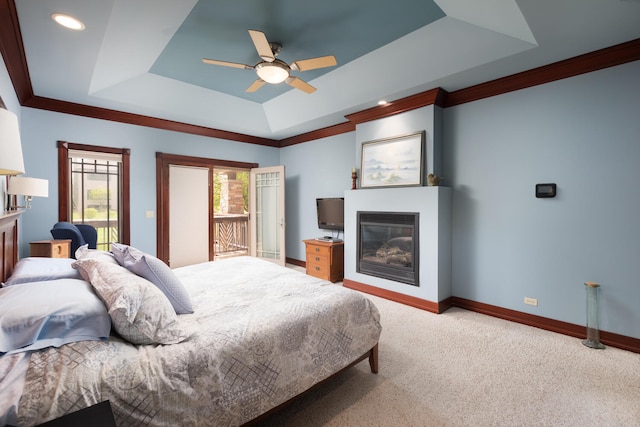 carpeted bedroom with crown molding, access to exterior, baseboards, a tray ceiling, and a large fireplace