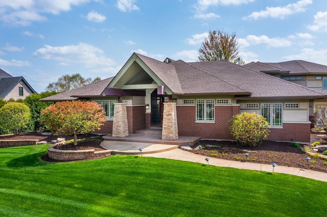 view of front facade with a shingled roof, a front lawn, and brick siding