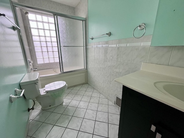 bathroom featuring tile walls, tile patterned floors, vanity, combined bath / shower with glass door, and toilet