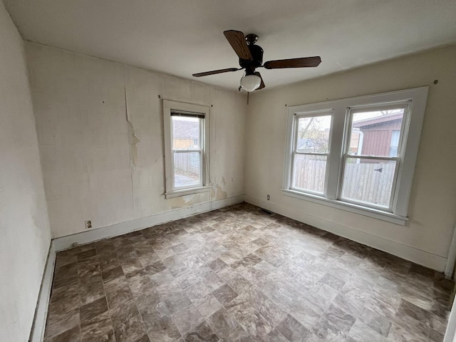empty room with baseboards, ceiling fan, stone finish floor, and a wealth of natural light