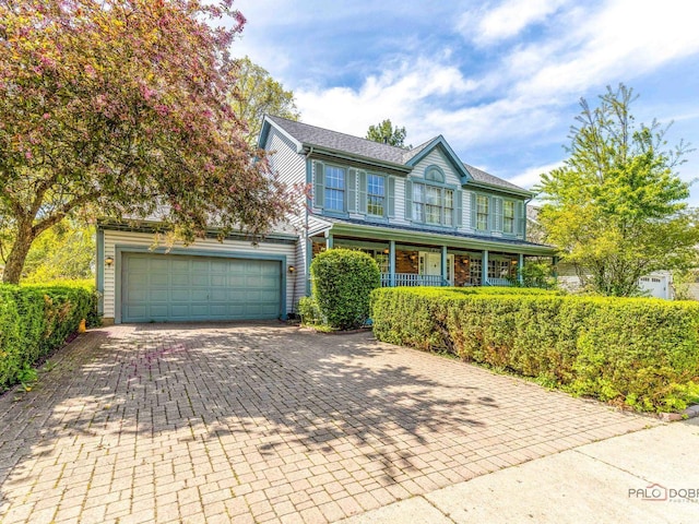 colonial-style house with a porch, decorative driveway, and a garage