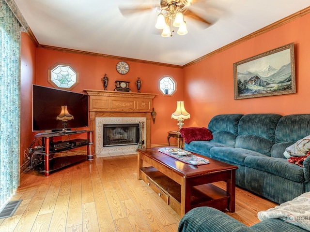 living room featuring light wood-style flooring, ceiling fan, a high end fireplace, and crown molding