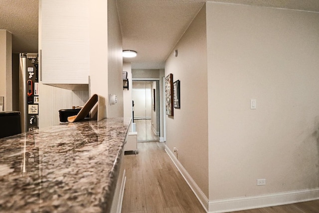 hallway featuring baseboards, a textured ceiling, and wood finished floors