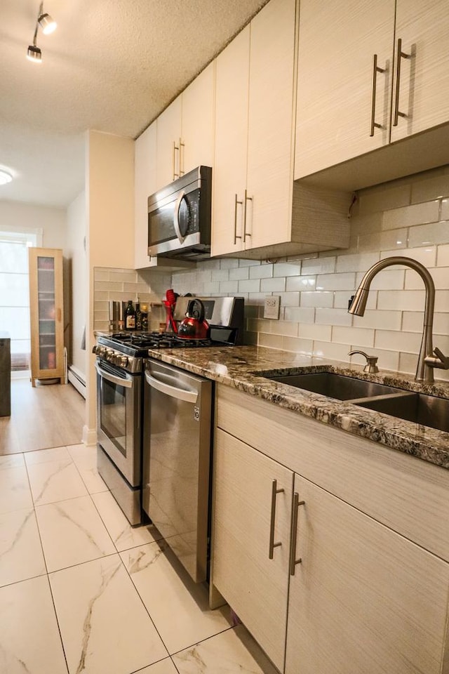 kitchen with backsplash, appliances with stainless steel finishes, baseboard heating, a sink, and marble finish floor