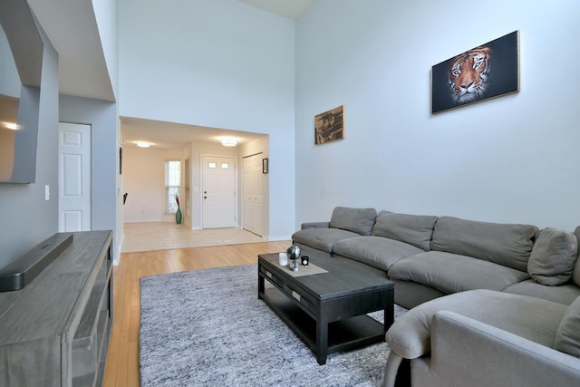 living area with light wood-style floors, baseboards, and a high ceiling