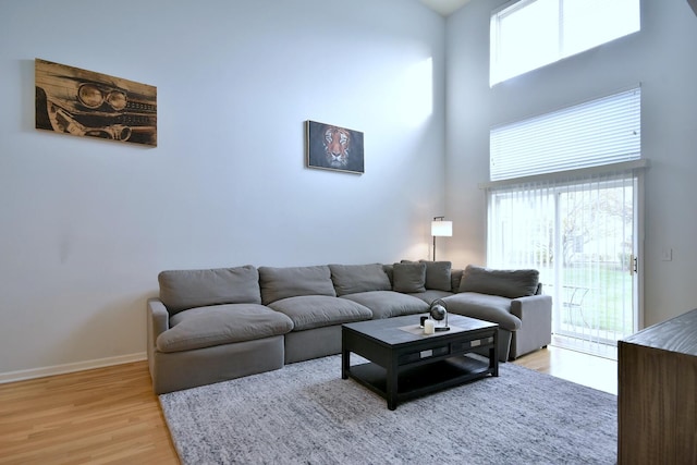 living room with light wood-style floors, baseboards, plenty of natural light, and a high ceiling