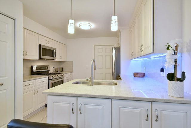 kitchen with a sink, stainless steel appliances, white cabinetry, a peninsula, and backsplash