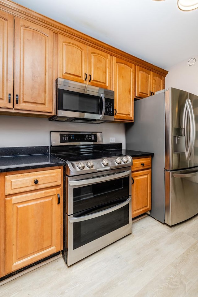 kitchen with appliances with stainless steel finishes, brown cabinetry, and light wood-type flooring