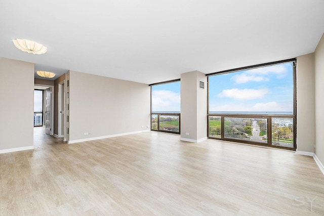 spare room featuring visible vents, baseboards, light wood finished floors, and floor to ceiling windows