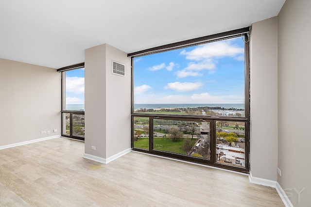 unfurnished room with a wall of windows, visible vents, wood finished floors, baseboards, and a water view