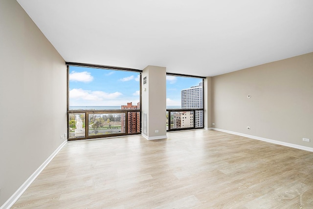 empty room with a wall of windows, baseboards, and light wood-style flooring