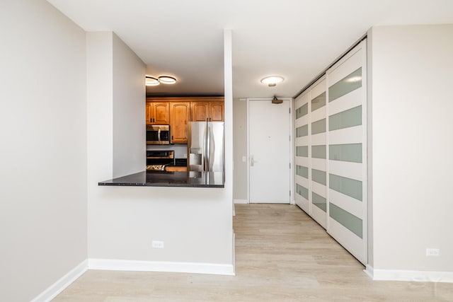 kitchen featuring dark countertops, baseboards, light wood-type flooring, brown cabinets, and appliances with stainless steel finishes