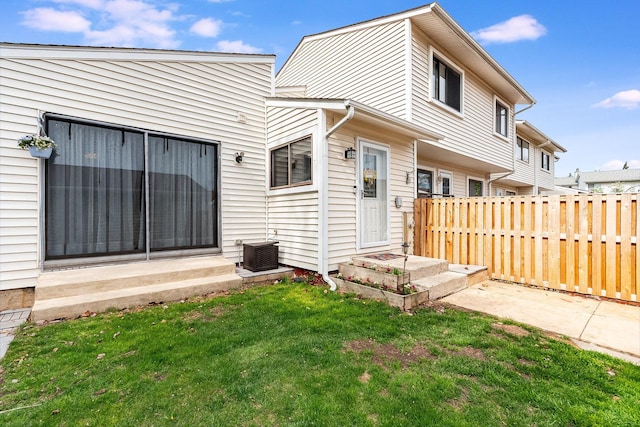 rear view of property featuring fence, central AC unit, entry steps, and a yard