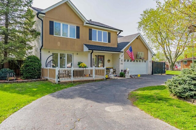 craftsman-style home featuring covered porch, driveway, a shingled roof, and a front lawn