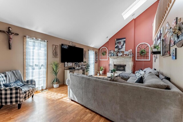 living room featuring high vaulted ceiling, a healthy amount of sunlight, light wood-style flooring, and a high end fireplace