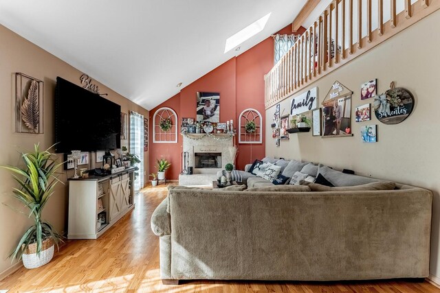 living area featuring a skylight, a fireplace, light wood-type flooring, high vaulted ceiling, and baseboards