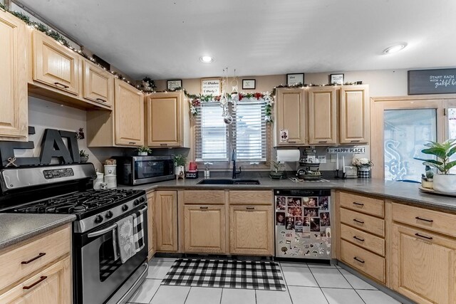 kitchen with dark countertops, appliances with stainless steel finishes, a sink, light brown cabinets, and light tile patterned floors