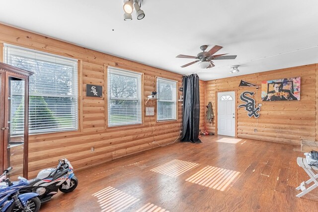 interior space featuring wood-type flooring, a ceiling fan, and wooden walls
