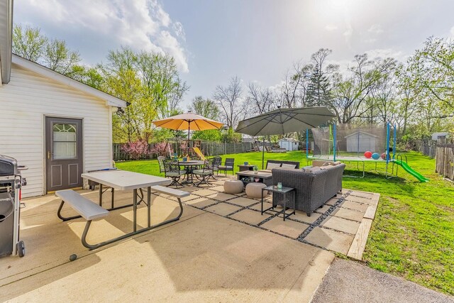 view of patio with a trampoline, an outbuilding, a fenced backyard, a storage unit, and outdoor dining space