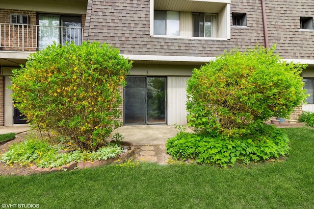 doorway to property with a lawn, a shingled roof, a balcony, and mansard roof