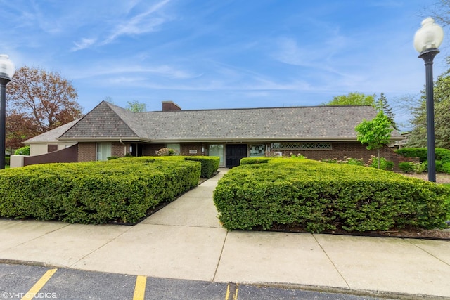 single story home featuring uncovered parking, brick siding, and a chimney