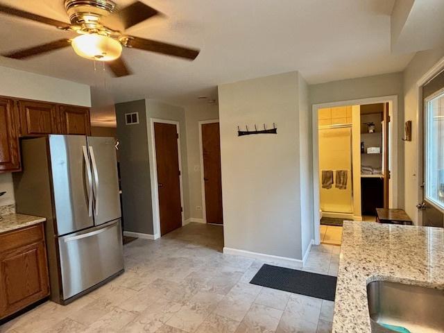 kitchen with a ceiling fan, visible vents, baseboards, light stone counters, and freestanding refrigerator