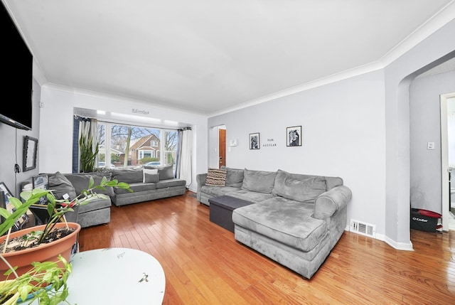 living area featuring arched walkways, ornamental molding, light wood finished floors, and visible vents