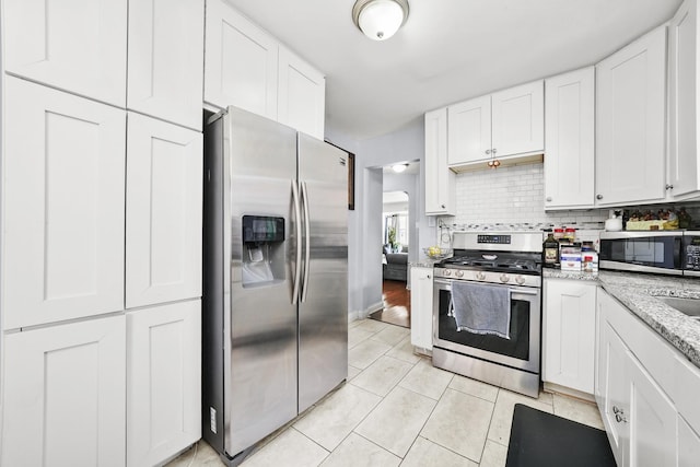 kitchen featuring tasteful backsplash, light stone countertops, light tile patterned floors, stainless steel appliances, and white cabinetry