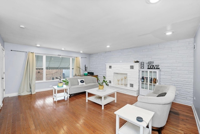 living room with baseboards, a stone fireplace, and wood finished floors