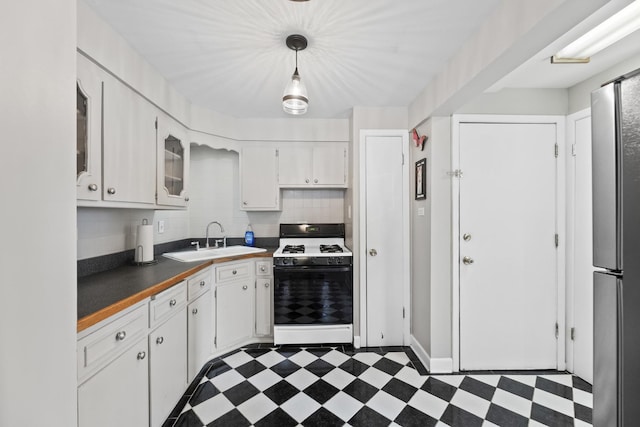 kitchen featuring freestanding refrigerator, gas range oven, white cabinets, dark floors, and a sink