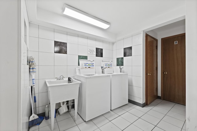 shared laundry area featuring washing machine and clothes dryer, light tile patterned flooring, and tile walls
