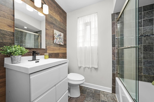 bathroom with stone finish flooring, baseboards, vanity, combined bath / shower with glass door, and toilet